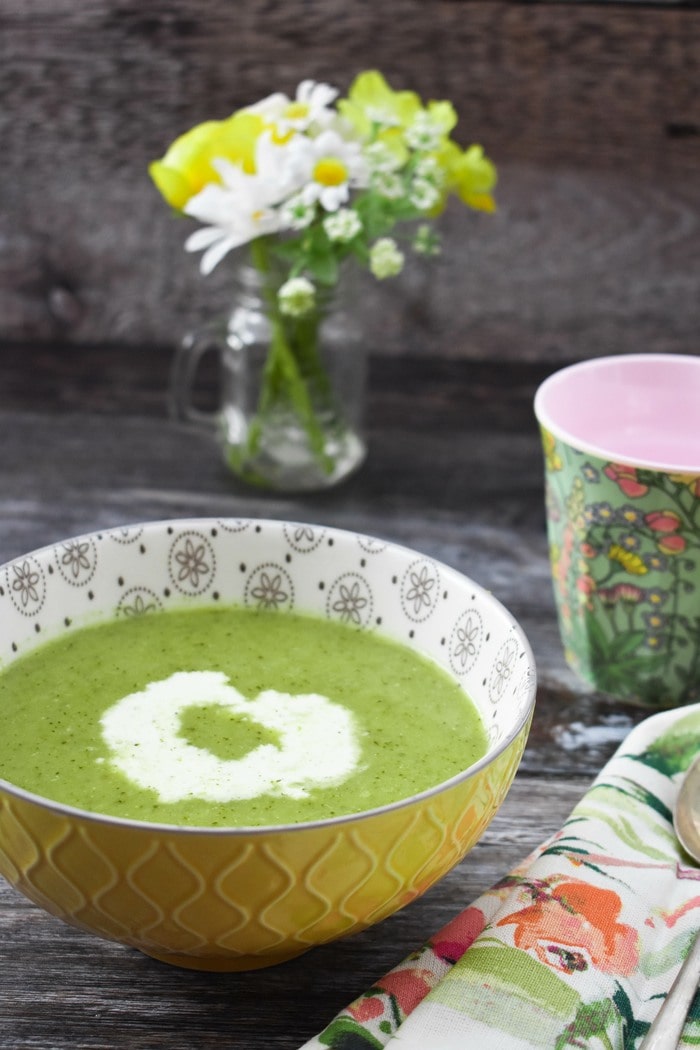 Low calorie broccoli and pea soup Broccoli soup in a yellow bowl next to a small vase of spring flowers