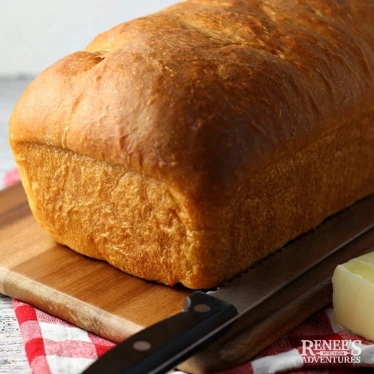 Whole loaf of soft white bread on a wooden board with knife ready to be sliced