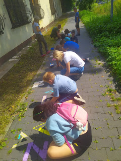 Dzieci rysujące kredą na chodniku.