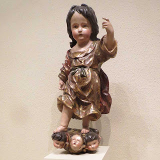 Wooden painted sculpture of a young child standing on disembodied heads of smaller children