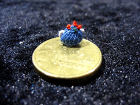 Tiny hand-knitted tea cosy displayed on an AU $2coin