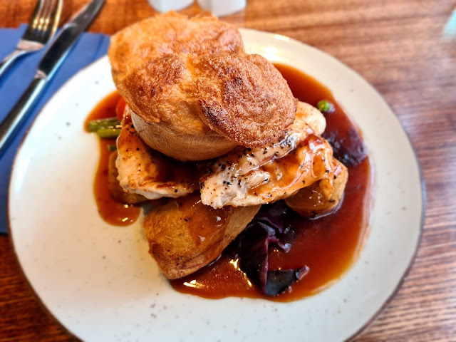 An overhead image of an entirely gluten free sunday roast dinner. The dinner is served on a white plate that is placed on a vintage oak table. The meal consists of roast chicken, vegetables, roast potatoes and yorkshire puddings.