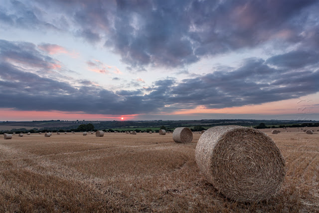 A Cotswold landscape filed with hay bales at sunset by Martyn Ferry Photography