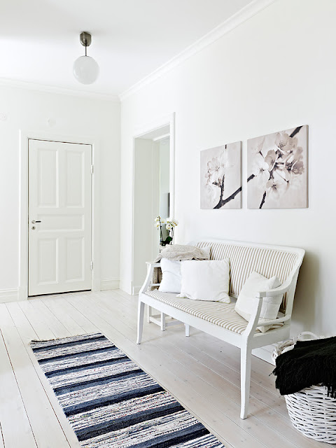 White Gustav style bench in a white foyer with a blue, white and black striped rug
