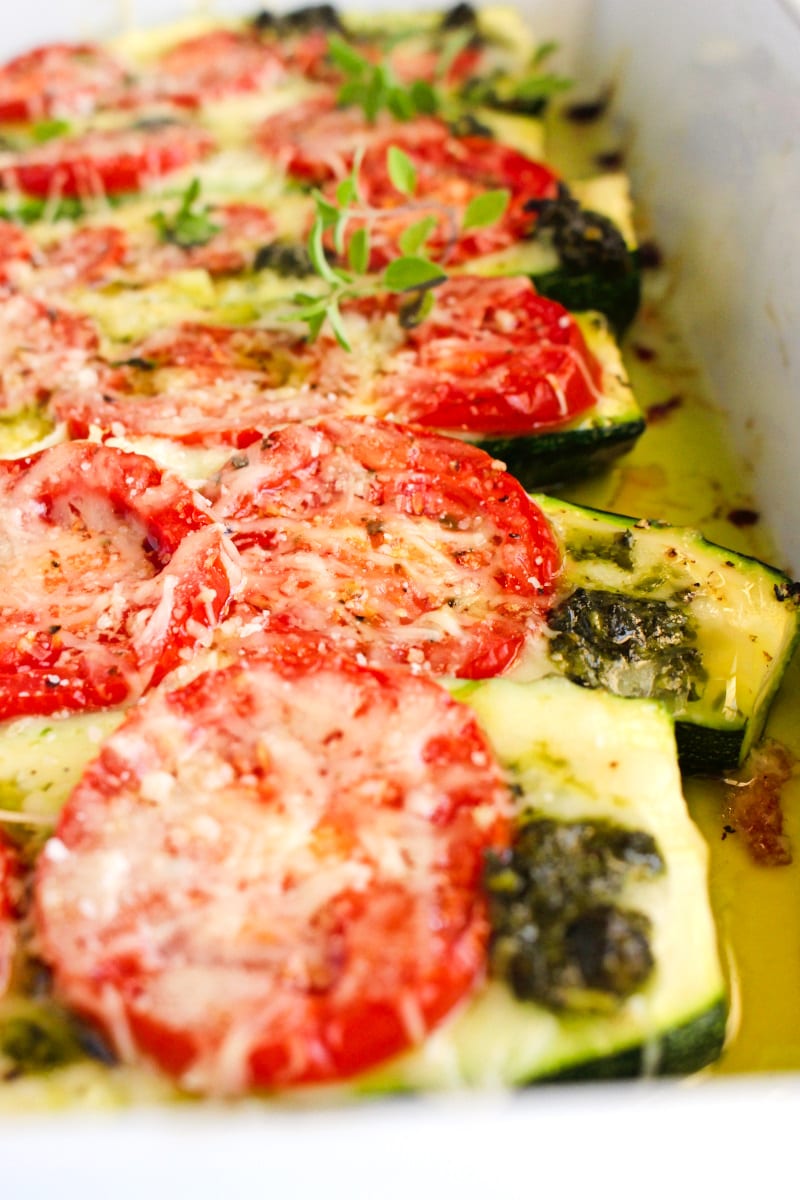 Closup side view of Tomato and Pesto Stuffed Zucchini Boats in a white glass baking dish.