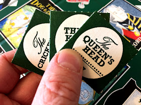 A hand of beer mat tokens from Inns & Taverns, including The Queen's Head.
