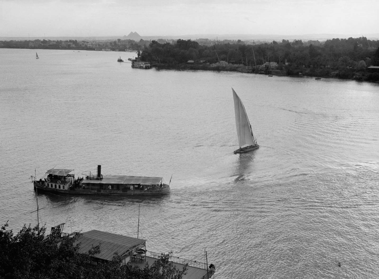 A steamship and sailboat cross paths on the Nile with the pyramids in the distance. 1920.