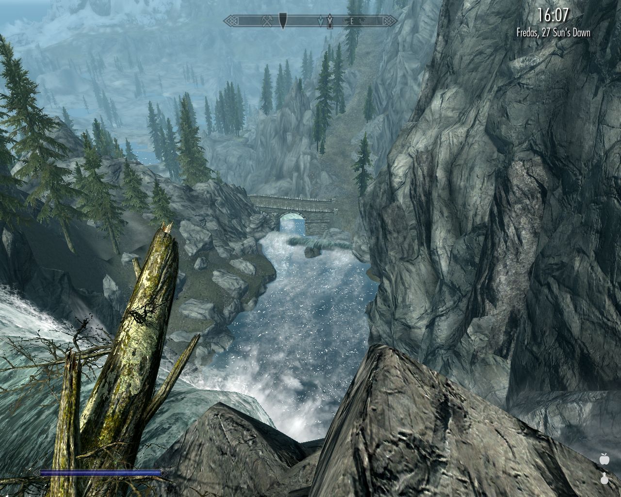 view from a rocky cliff down a waterfall, foaming blue river leads to a stone bridge in the distance