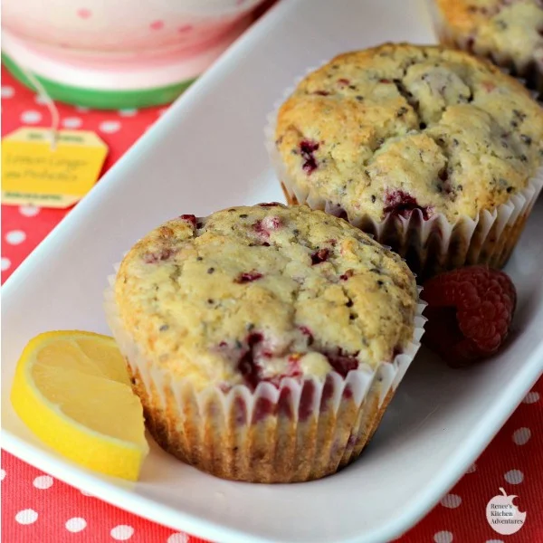 Lemon Raspberry Chia Seed Muffins by Renee's Kitchen Adventures sitting on a white platter with lemon and raspberry garnish with a cup of hot tea in the background 