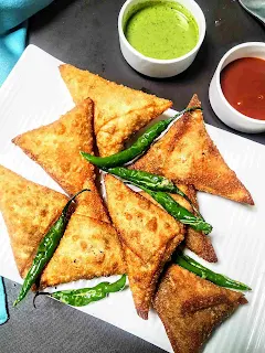 Onion samosa with fried green chili. Green chutney and sweet chutney in background
