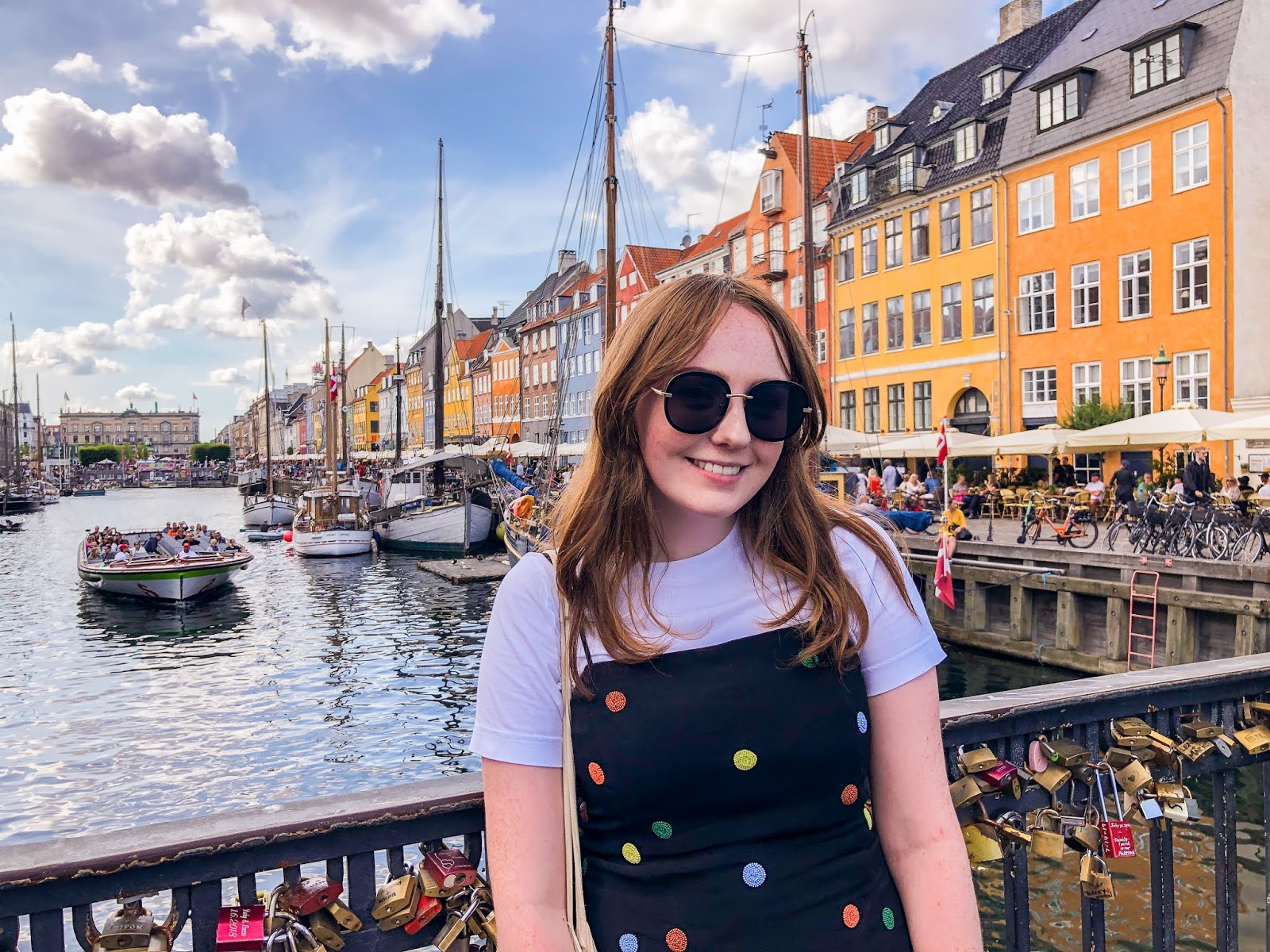 Copenhagen travel itinerary: smiling travel blogger smiles on bridge at nyhavn, with coloured houses in background