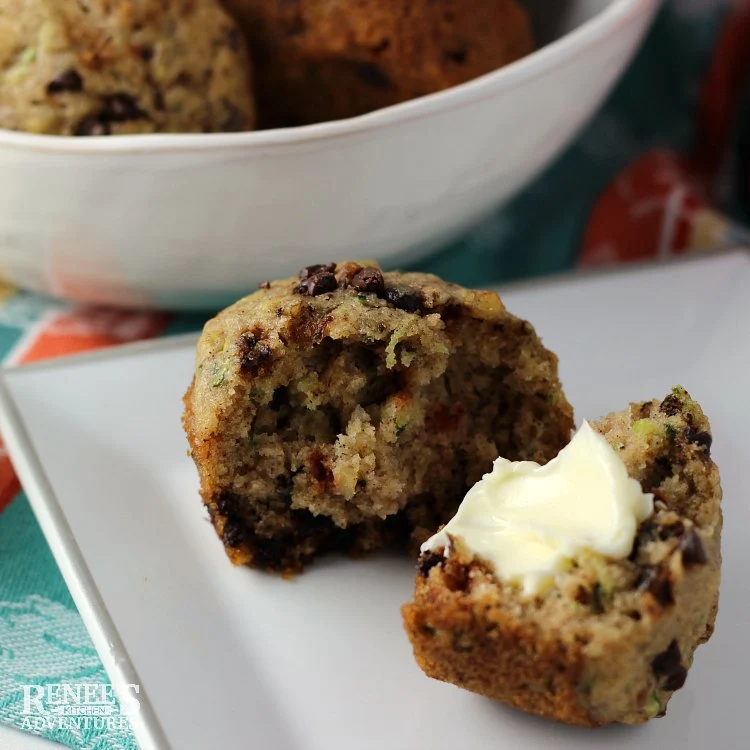 Chocolate Chip Zucchini Muffins by Renee's Kitchen Adventures muffin cut open with butter on one half with bowl of muffins in the background