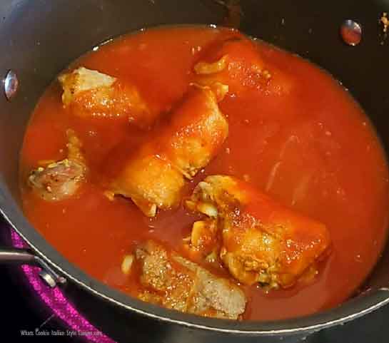 this is a pan of braciole stuffed meat rolls simmering in tomato sauce