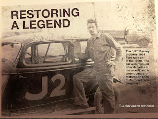 Sam Massey stands next to the 1934 Ford race car in this yellowed vintage photo. He is wearing coverall with his foot on running board. His name is above door on roof.