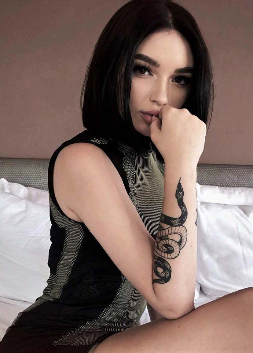 Vemos la image de una joven sensual, con un tatuaje de linea fina de serpiente en el antebrazo