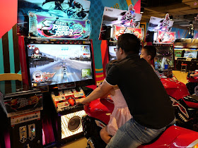 daughter riding a fake motorcycle with father as he plays the Speed Rider 2 video game