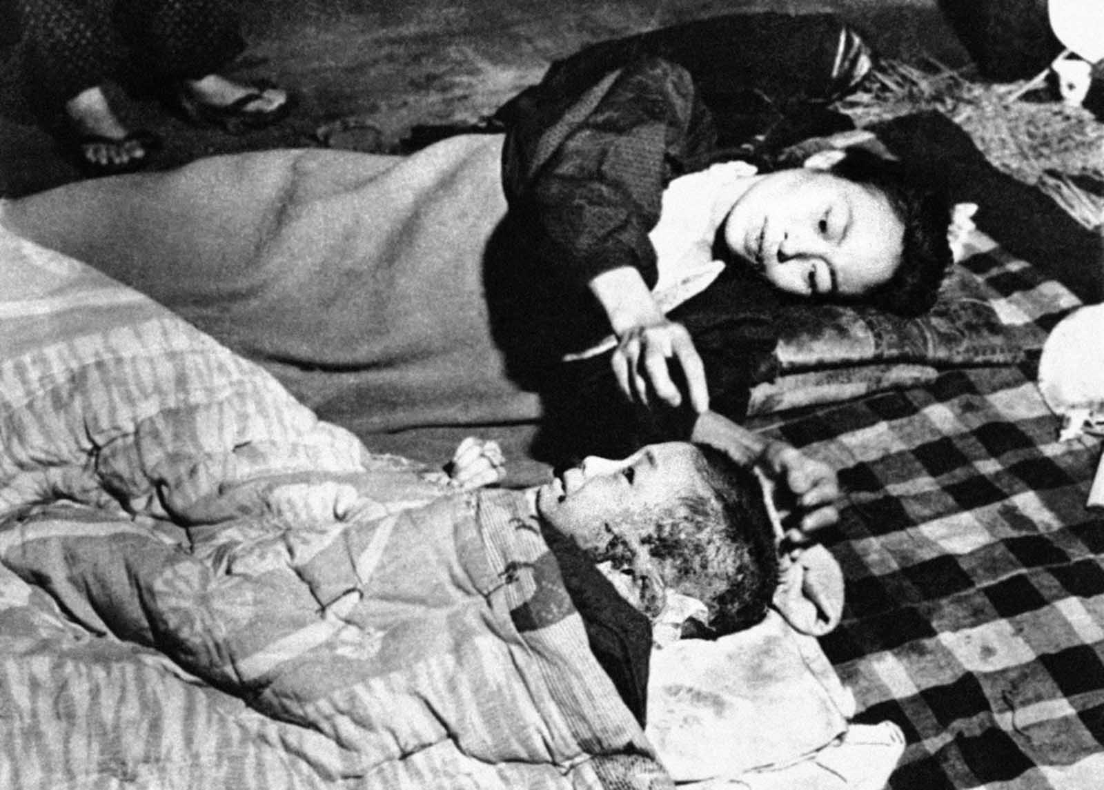 A Japanese woman and her child, casualties in the atomic bombing of Hiroshima, lie on a blanket on the floor of a damaged bank building converted into a hospital and located near the center of the devastated town, on October 6, 1945.