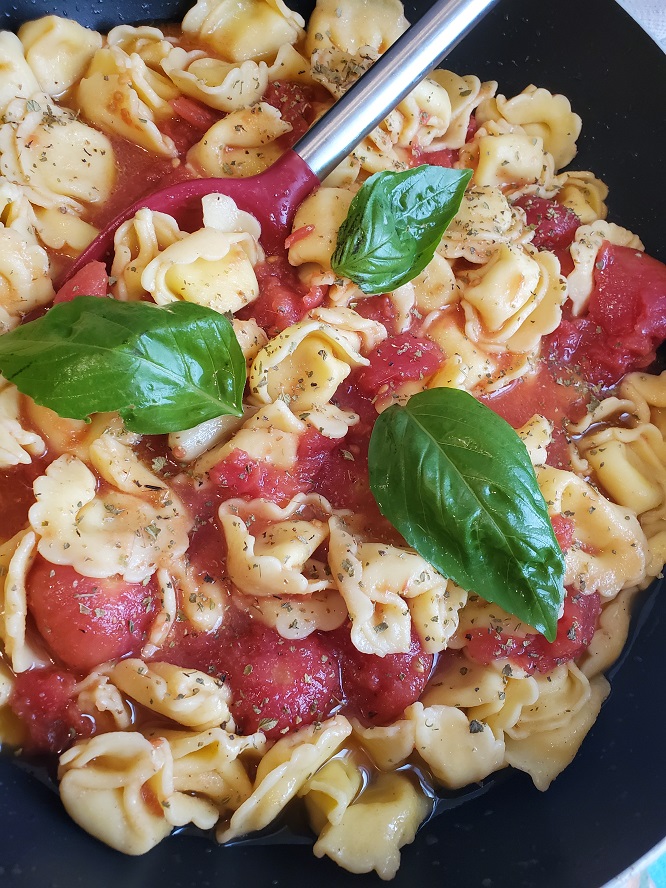 This is fresh tortellini pasta with Italian dressing, mozzarella, tomatoes and fresh basil on top in a white pasta dish