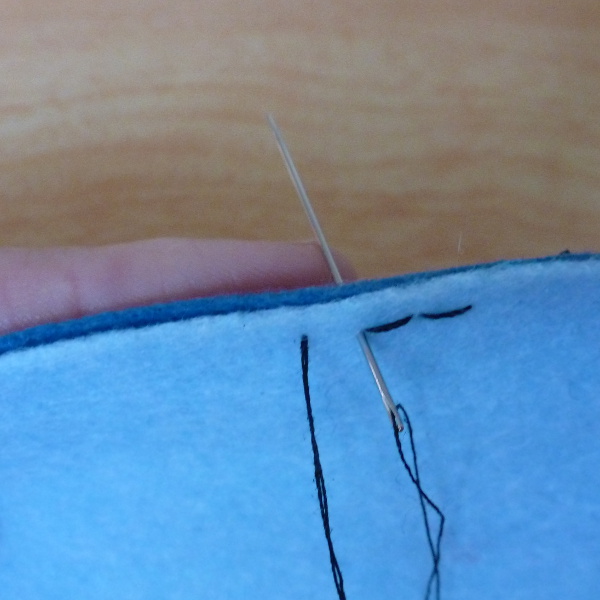 Using a finger as a guide to steady the needle at the back edge of the fabric