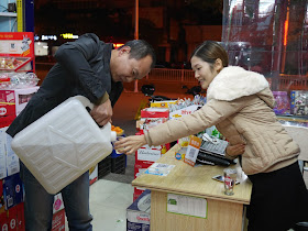 man pouring mijiu from a large plastic jug into a plastic cup held by a woman at a store in Xiapu, China