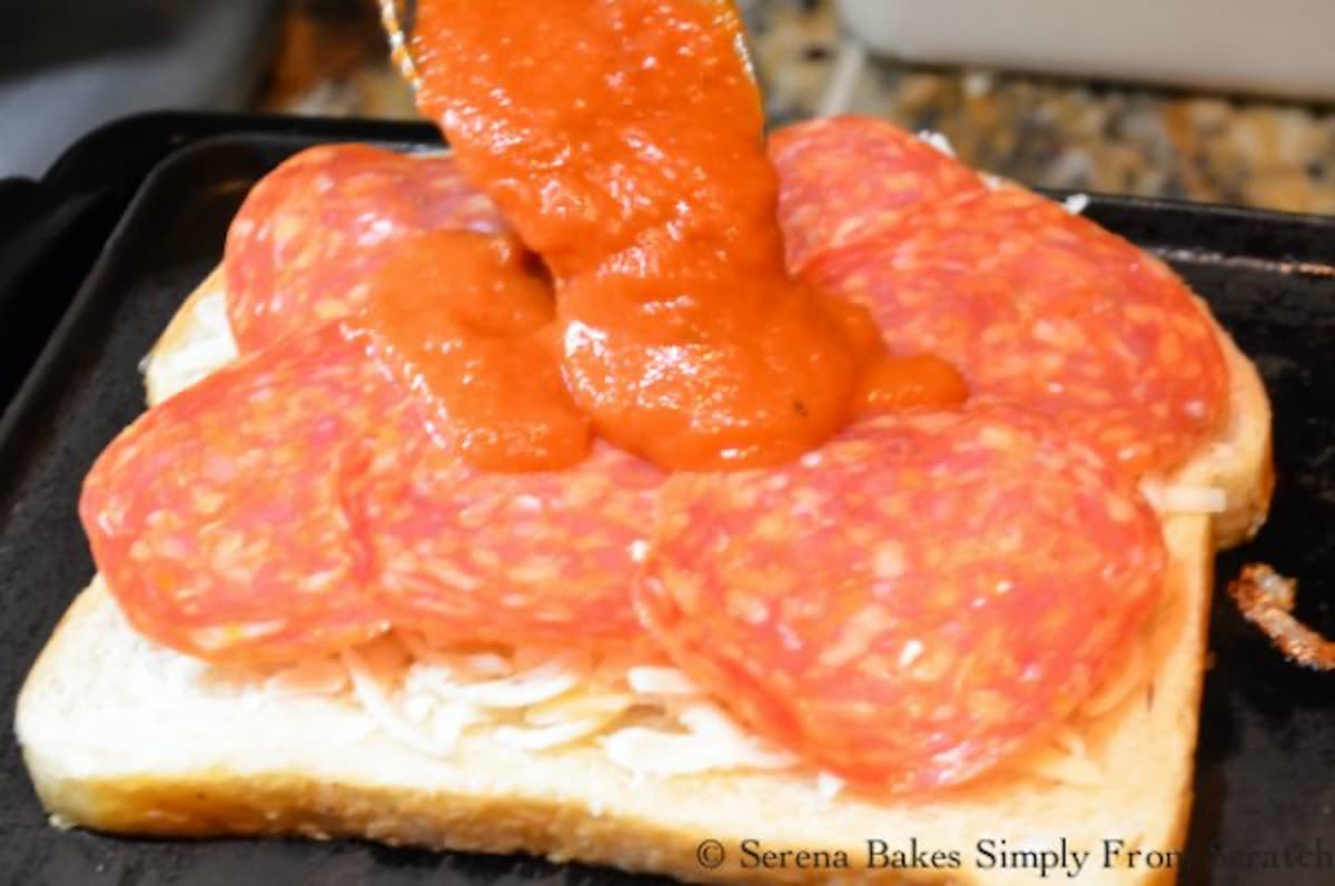 Pizza Sauce being spread on top of pepperoni to make Pepperoni Pizza Grilled Cheese Sandwiches.