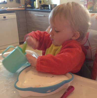 toddler in highchair happily stirring cup with spoon