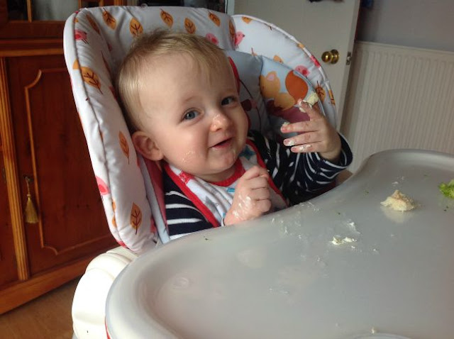 Baby in highchair eating food on face and hands