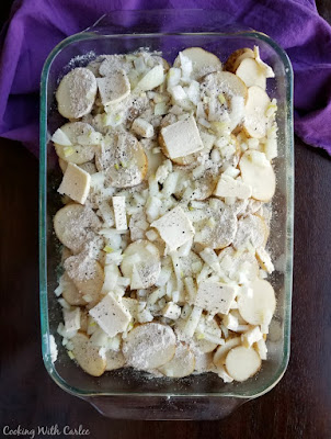 glass casserole dish filled with sliced potatoes, butter and onions