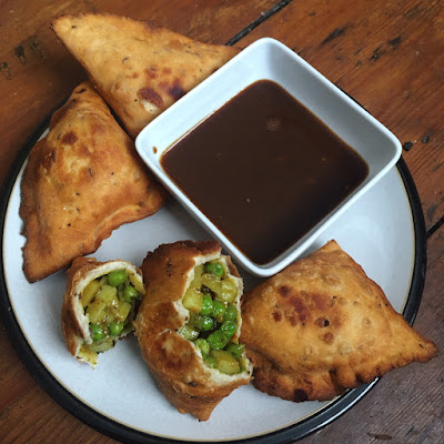 A plate with four samosas on. One is broken in half to show the potato and pea filling.