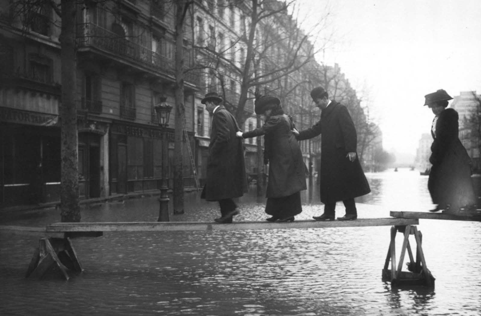 People gingerly cross the street on a wooden plank.