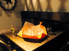 Interior of a modern dolls' house miniature cafe at night, with two glasses of wine and an unwrapped gift on the table.