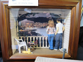 One-twelfth scale miniature scene of a woman and a man on a porch looking over a harbour view at night.