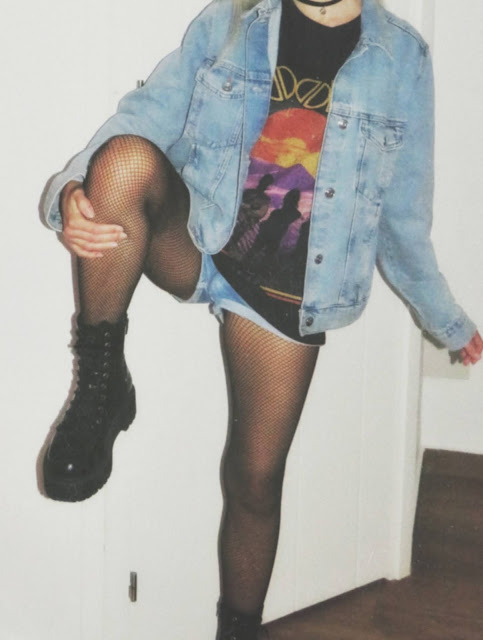 Estilo grunge con camiseta negra ancha con imagen del grupo The Doors, pantalón corto, medias de red pequeña, botas estilo militar y cazadora vaquera