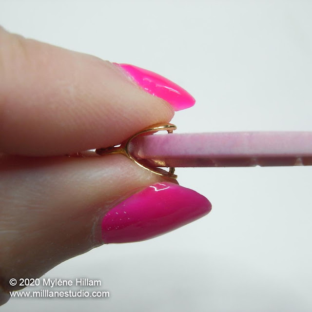 Squeezing the prongs of a silver pinch bail into a thin pink resin casting
