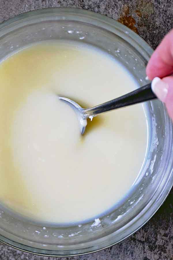 Melted white chocolate and cream in a bowl for Raspberry White Chocolate Cheesecake filling