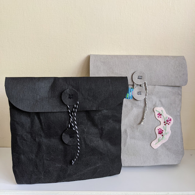 2 paper fabric envelope pouches with two circles stitched on the front and flap with a string closure