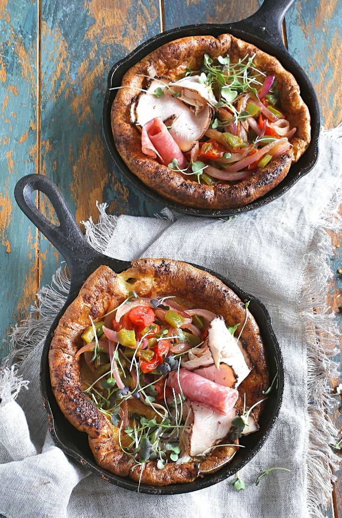 Recipe for a savory Dutch baby German pancake filled with cheese and topped with sauteed bell peppers, red onions, tomatoes and ham.