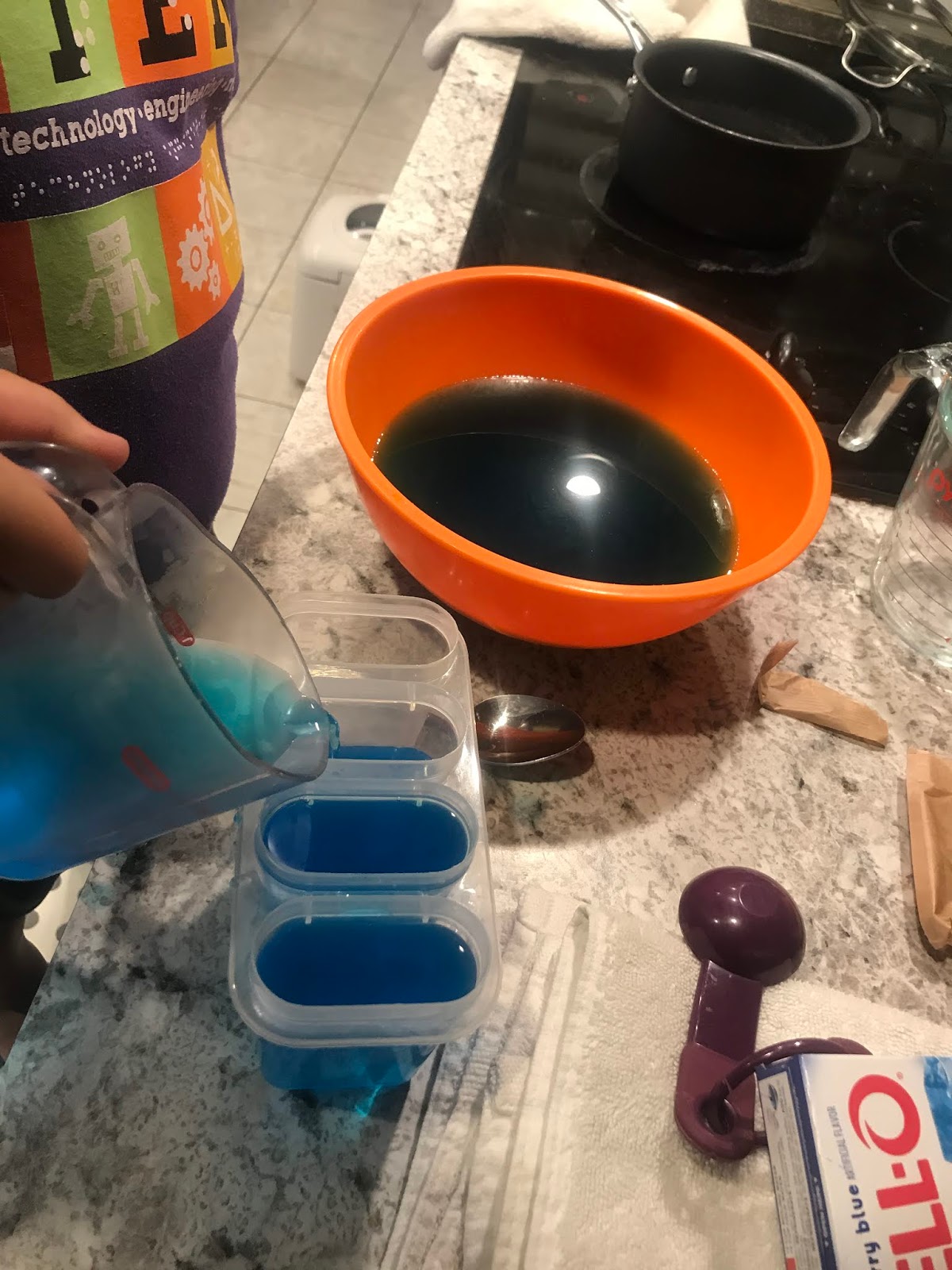 a close up of a girl's hand as she uses a small measuring cup to pour liquid into mold