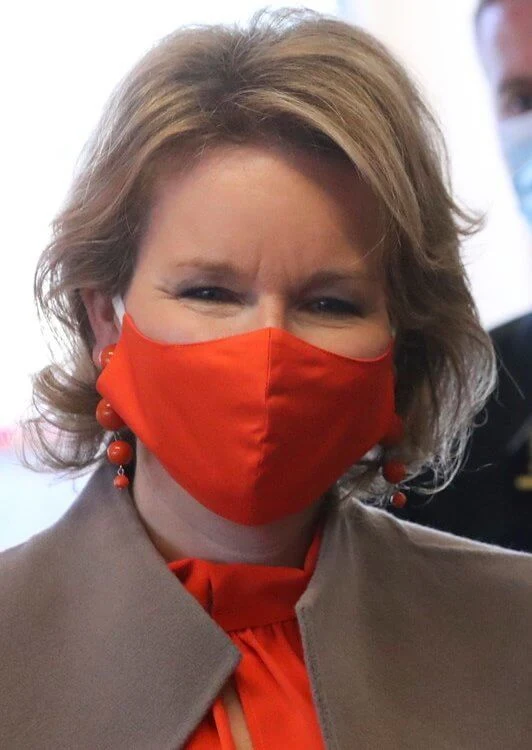 Queen Mathilde wore an orange color silk top and mask from Natan, and a beige wool coat by Natan. the pharmacy Pharma Haelvoet in Evere