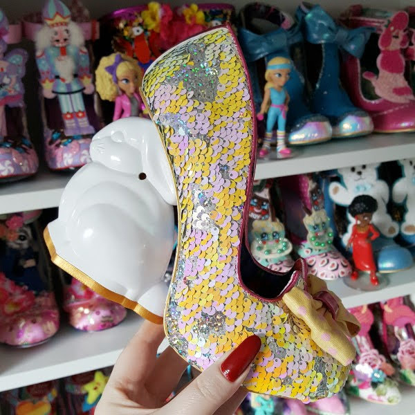holding yellow sequins court shoe with bunny shaped heel in hand in front of shoe shelves