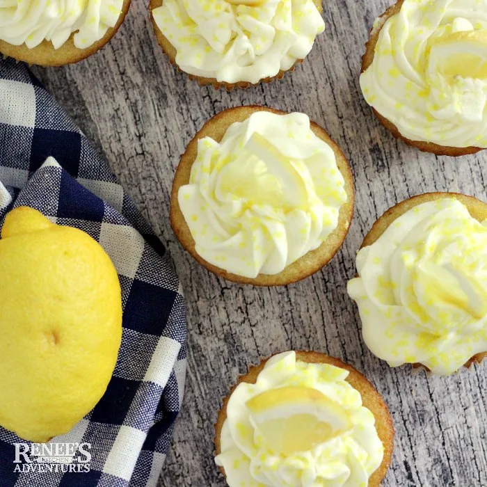 Easy Lemon Cupcakes by Renee's Kitchen Adventures overhead shot with cupcakes scattered on a board with a blue and white checked towel with lemons on it to the left