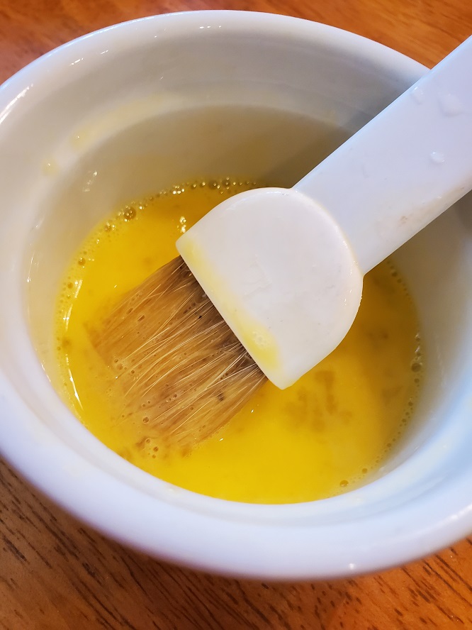 this is raw beaten eggs with a brush in a white bowl
