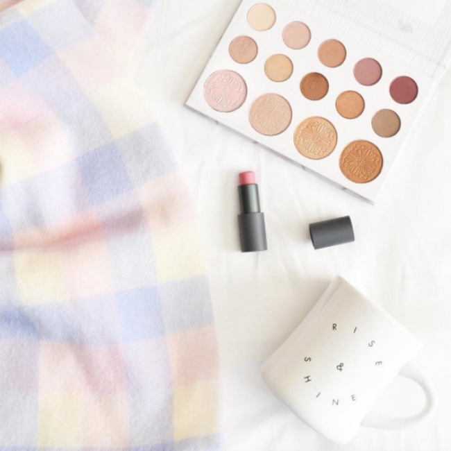 A flat lay featuring a plaid scarf, the carli bybel eyeshadow and highlighter palette, a bite multistick in macaroon, and a mug from popsugar must have box.