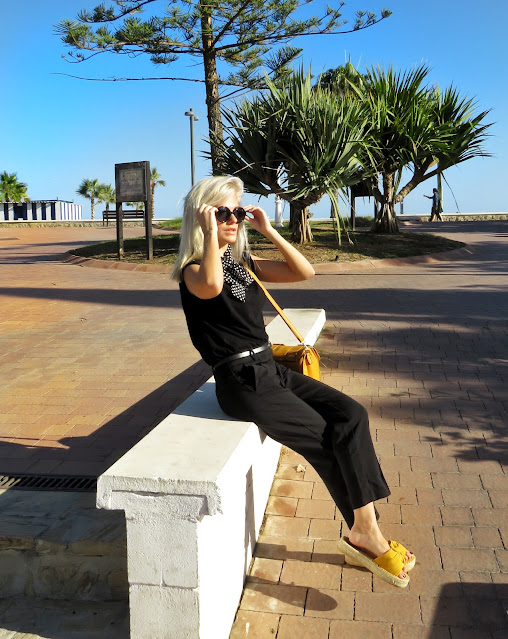 Alejandra Colomera con camiseta negra, pantalón formal negro, lazo en el cuello negro con lunares blancos y complementos mostaza