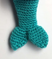 A close up of a crocheted mermaid's tail in teal 4-ply yarn. Te tail has two fins at the bottom.