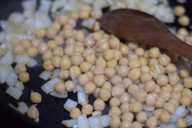 The can of chickpeas being added to the skillet with the diced onion and minced garlic. 
