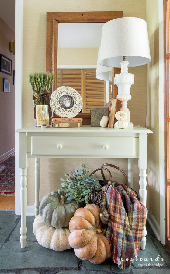 small white table with large pumpkins and plaid blanket scarf in a basket