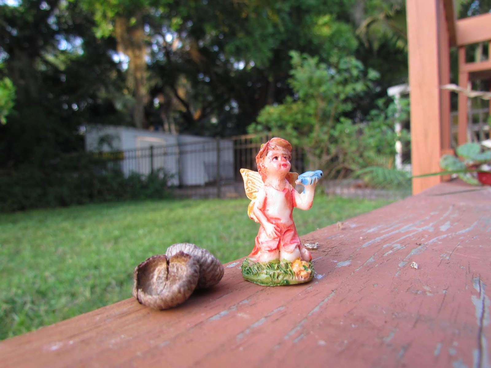 A tiny boy fairy statue holding a bird in the garden on a porch with an acorn