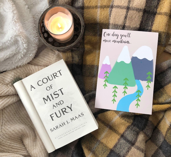 Overdue July reading wrap up! Title page of 'A COurt of Mist and Fury' next to a candle and art print of a mountain
