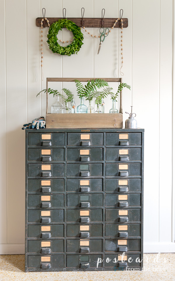 vintage metal industrial cabinet with wooden toolbox and fern branches in vintage glass bottles